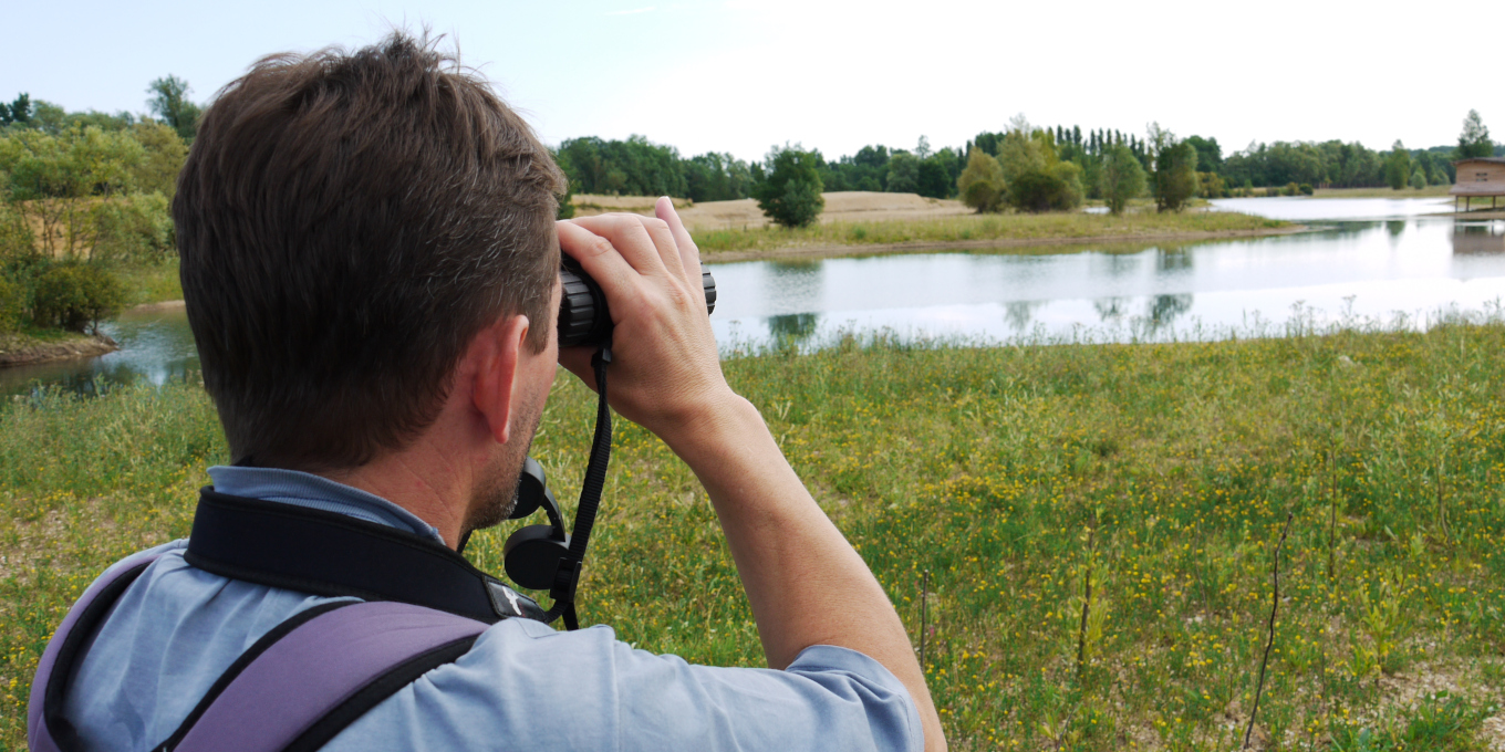 Un homme observe aux jumelles des oiseaux au bord du plan d'eau de Saint-Cyr